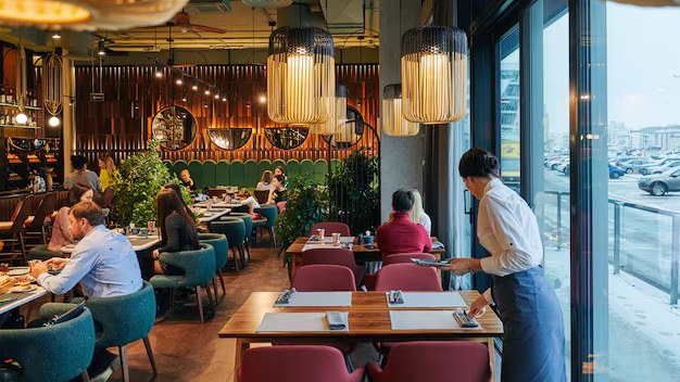 Sala de um restaurante acolhedor com clientes à mesa e um empregado de mesa a servir.