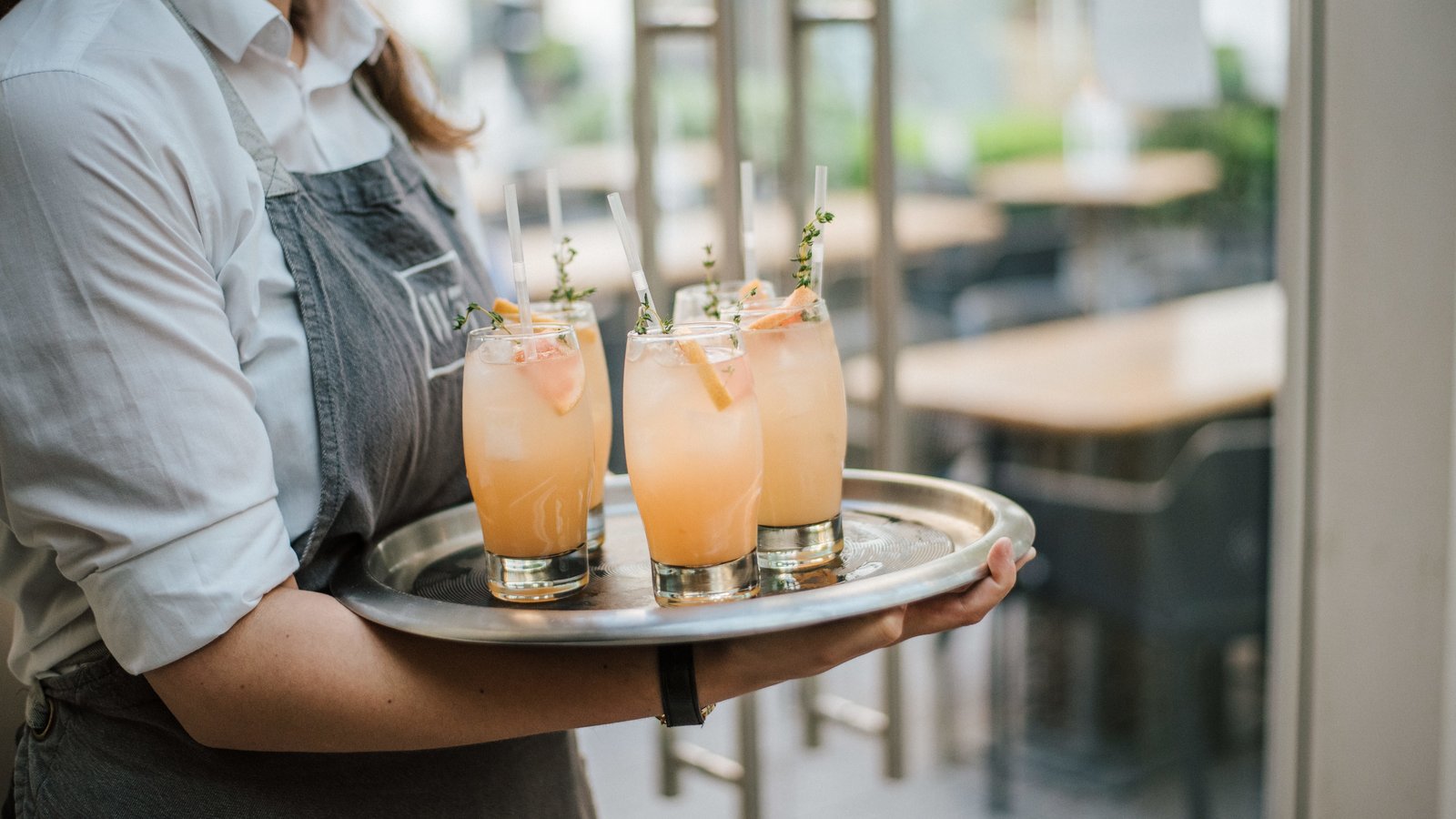Empregado de mesa a servir um tabuleiro com cocktails de laranja fresca numa esplanada de restaurante.