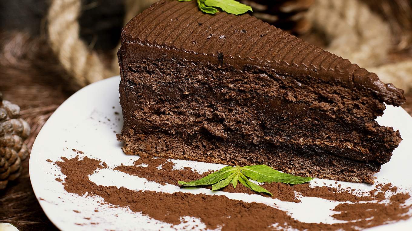 Fatia de bolo de chocolate emplatada com folhas de hortelã, exemplo de fotografia profissional de prato.