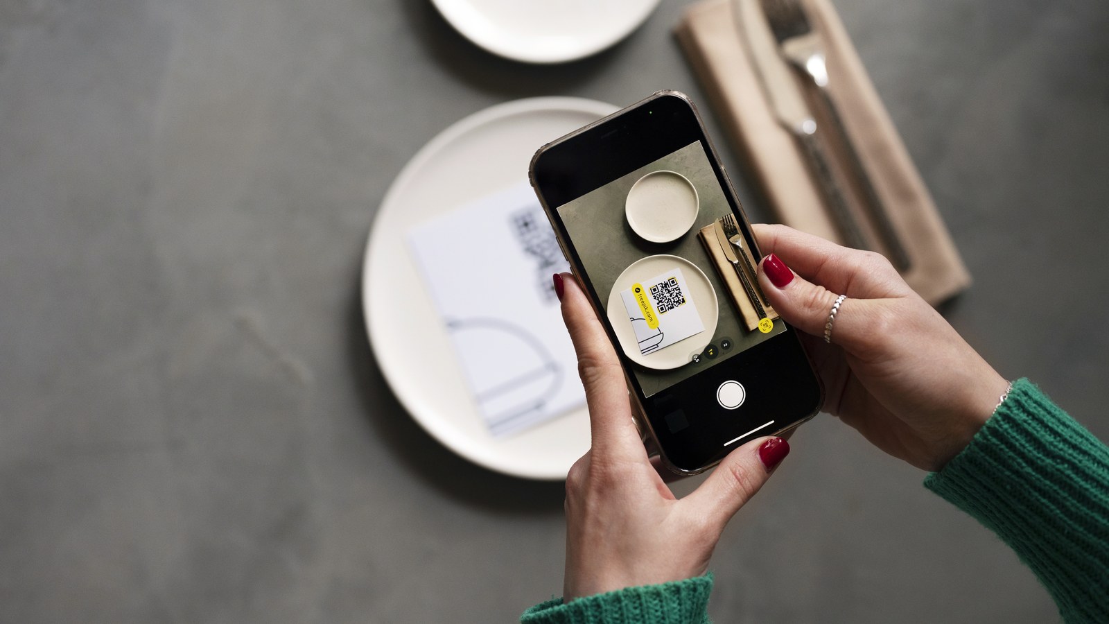 Mãos a segurar um telemóvel para ler um código QR pousado sobre a mesa de um restaurante.